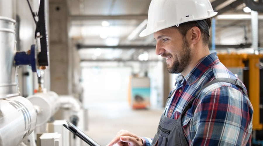 Man in hard hat using tablet to monitor HVAC systems in commercial setting, emphasizing advanced technology and efficiency in air quality management.